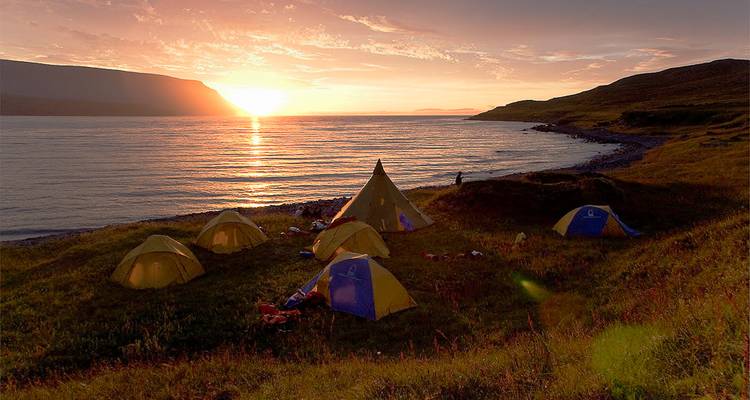 Coastal campsite at sunset with glowing sky reflecting on calm fjord waters