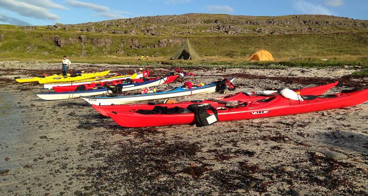 Colourful sea kayaks lined up on a rocky Icelandic beach with tents in background