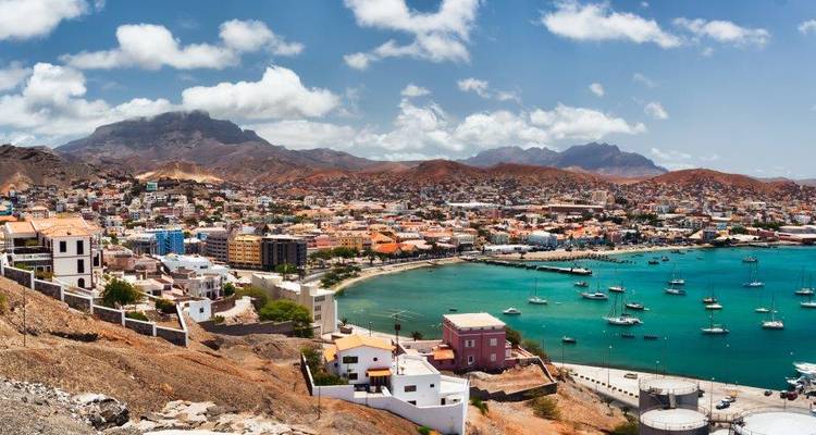 Vue panoramique du port de Mindelo avec ses maisons colorées, son marina et ses montagnes arides sous des nuages épars.