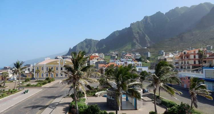 Ville côtière avec des palmiers et des maisons colorées nichée au pied de montagnes vertes escarpées.