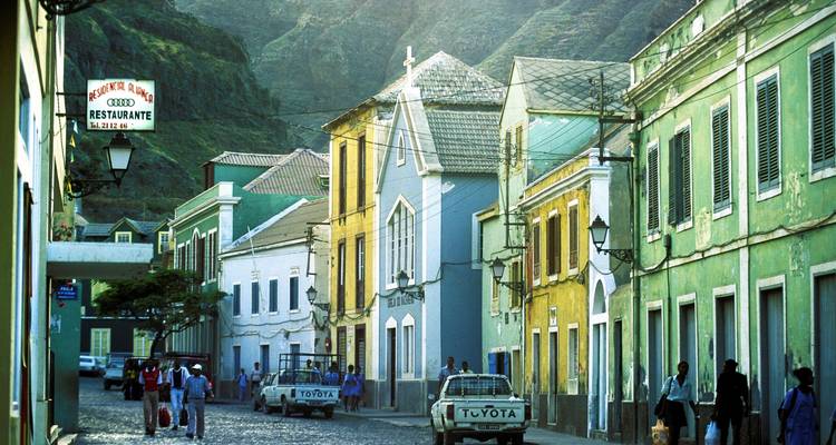 Rue principale animée de Ribeira Grande bordée de bâtiments coloniaux colorés avec des montagnes qui s'élèvent en arrière-plan.