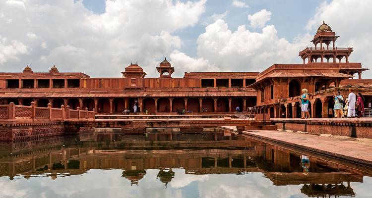 Innenhof aus rotem Sandstein und Wasserbecken in Fatehpur Sikri mit kleinen Besuchergruppen unter einem teilweise bewölkten Himmel.