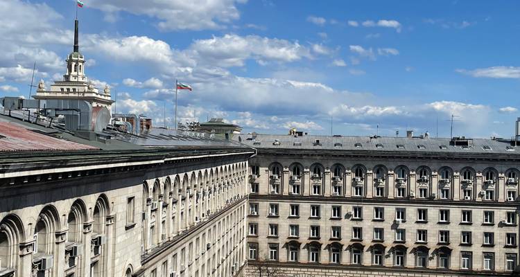 Bâtiments gouvernementaux de Sofia avec des drapeaux bulgares sous un ciel bleu éclatant et des nuages cotonneux.
