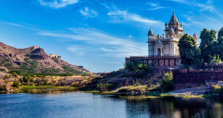 Weißer Marmor-Kenotaph neben einem ruhigen See mit Festungsmauern, die sich über felsige Hügel erstrecken.