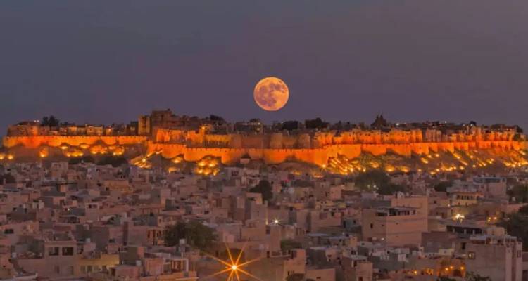 Der Vollmond erhebt sich über den golden beleuchteten Festungswällen des Jaisalmer Forts, das nachts das Stadtbild der Wüste beherrscht.