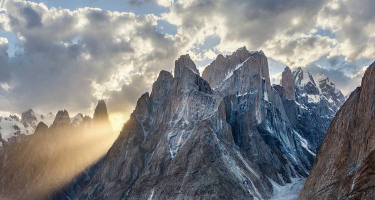 Dramatische zerklüftete Granitspitzen fangen einen goldenen Sonnenstrahl unter stimmungsvollen Wolken ein.