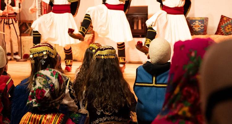 Des enfants assis portant des foulards colorés regardent un spectacle de danse folklorique en Albanie.