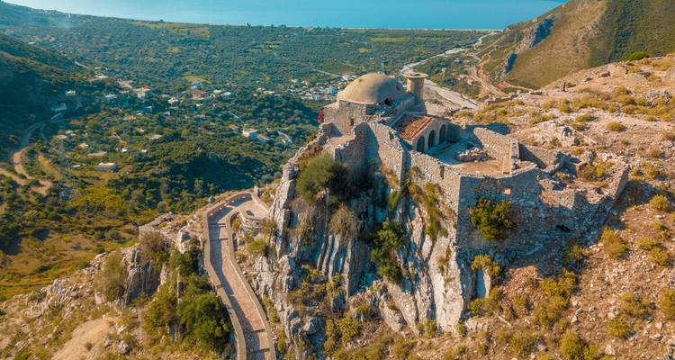 Vue aérienne de ruines d'une ancienne forteresse au sommet d'une colline dominant la mer Ionienne et une vallée verdoyante.