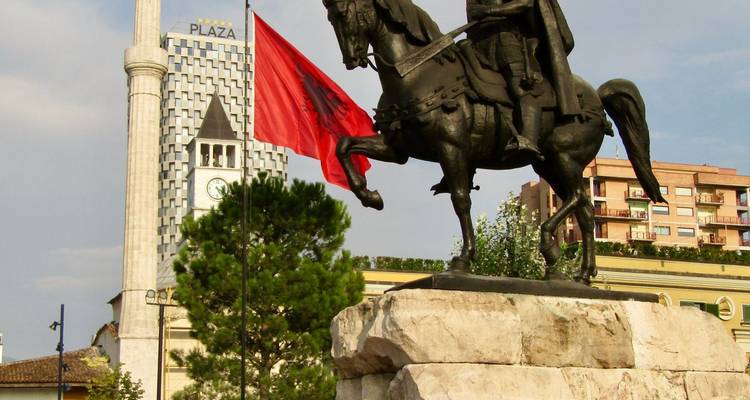Statue équestre de Scanderbeg sur un piédestal en marbre avec le drapeau albanais et une tour de l'horloge.