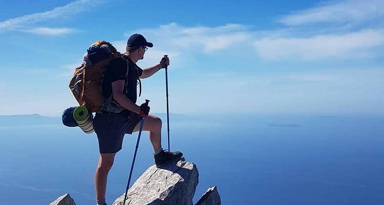 Routard solitaire debout sur un étroit piton rocheux surplombant une vaste mer bleue et le ciel.