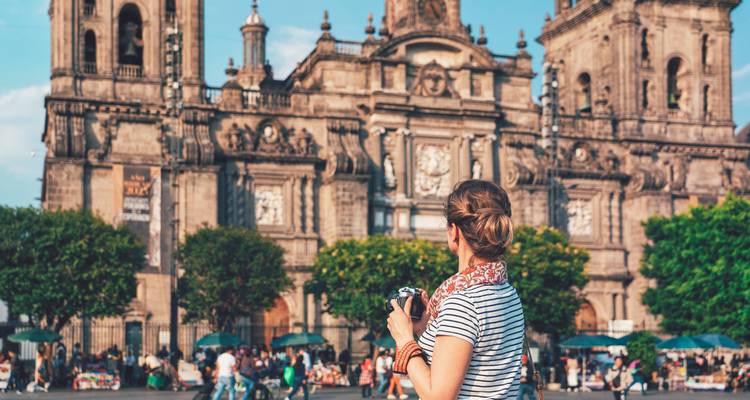 Voyageur tenant un appareil photo contemple la façade ornée de la cathédrale de Mexico sur la place.