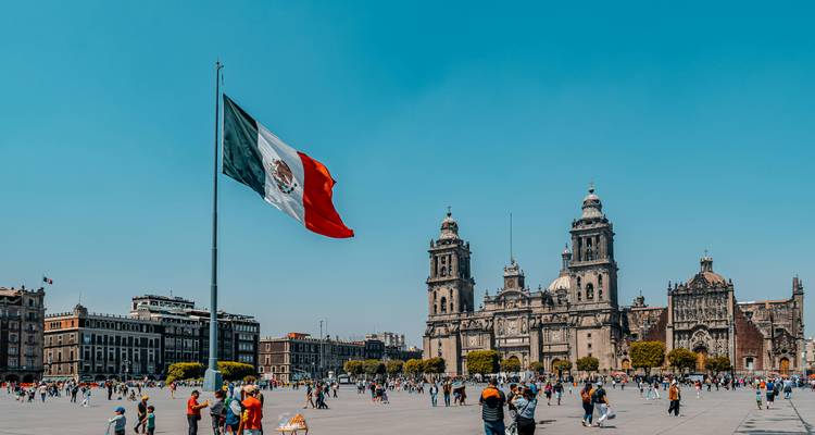 Vue panoramique de la place principale de Mexico bondée de visiteurs, cathédrale et drapeau imposant sous un ciel dégagé.