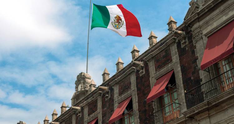 Gros plan d'un bâtiment historique en pierre avec des auvents rouges et un drapeau mexicain qui flotte au-dessus.