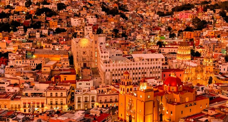 Luchtfoto in de schemering van Guanajuato's dicht opeengepakte kleurrijke gebouwen en verlichte universiteit en basiliek.