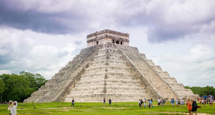 La pyramide El Castillo à Chichen Itza entourée de visiteurs sur des terrains luxuriants sous des nuages dramatiques.