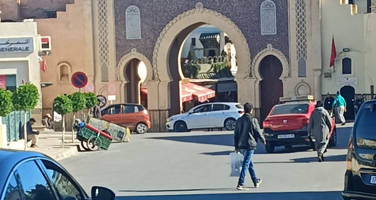 Escena callejera en la puerta de Bab Bou Jeloud en Fez con coches y peatones.