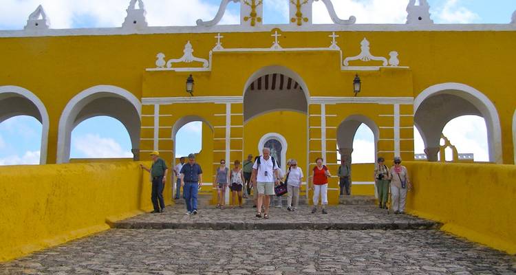 Des touristes descendent une rampe pavée vers les arches jaune vif du couvent d'Izamal