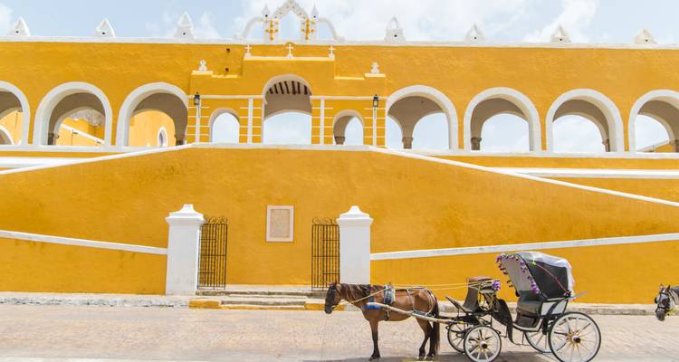 Une calèche tirée par un cheval attend près des murs et arches jaune vif de la place du couvent d'Izamal