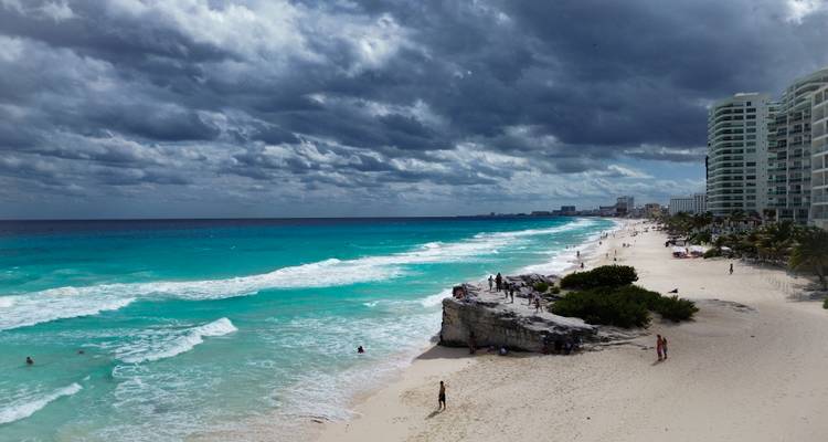 Les vagues turquoise se brisent sur une plage de sable blanc de Cancún avec des complexes hôteliers et de spectaculaires nuages d'orage au-dessus