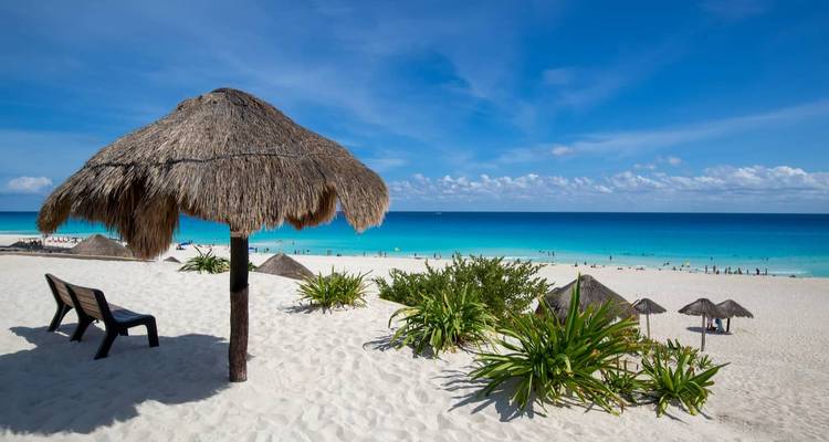 Large plage de sable avec parasol en palapa, chaises longues et eaux turquoise des Caraïbes sous un ciel dégagé