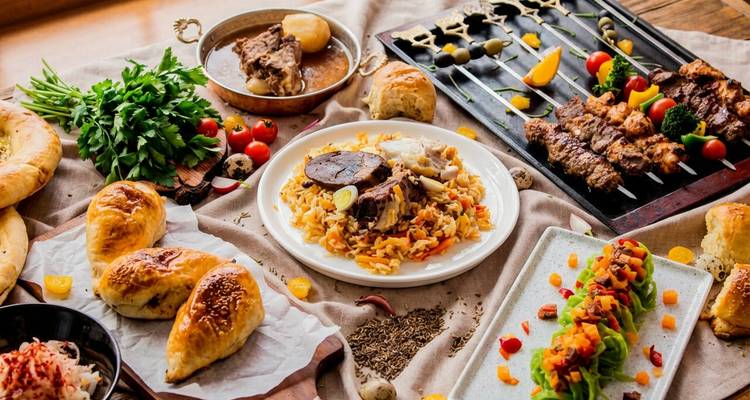 Colorido despliegue de platos uzbekos que incluye plov, pasteles samsa, hierbas frescas y brochetas de shashlik a la parrilla dispuestos sobre una mesa rústica.