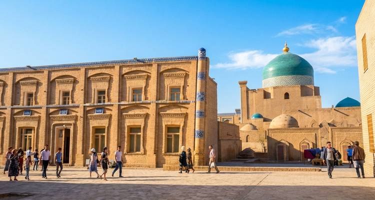 Los visitantes caminan por una calle iluminada por el sol de madrasas color adobe coronadas por una cúpula turquesa en el casco antiguo de Khiva.