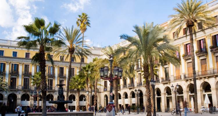 Zonnige dag op Plaça Reial in Barcelona met palmbomen, historische arcades en een centrale fontein.