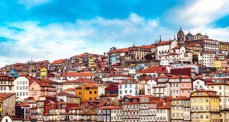 Kleurrijke heuvelflank met historische gebouwen in Porto onder een gedeeltelijk bewolkte blauwe hemel.