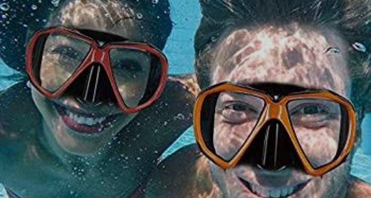 Two snorkelers smile underwater wearing colorful dive masks, surrounded by shimmering light.
