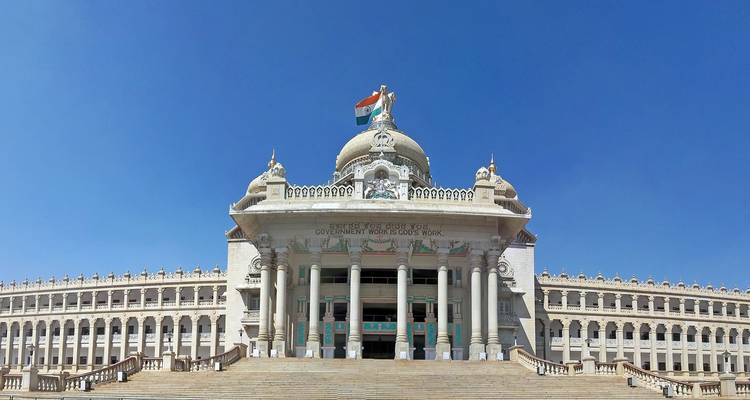 The stately Vidhana Soudha building under a cloudless blue sky with the Indian flag aloft.