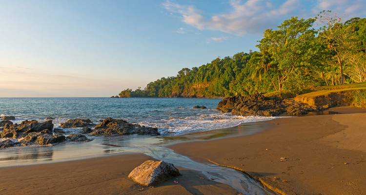 Ruhiger tropischer Strand mit dschungelbedeckter Landzunge und sanften Wellen zur goldenen Stunde.