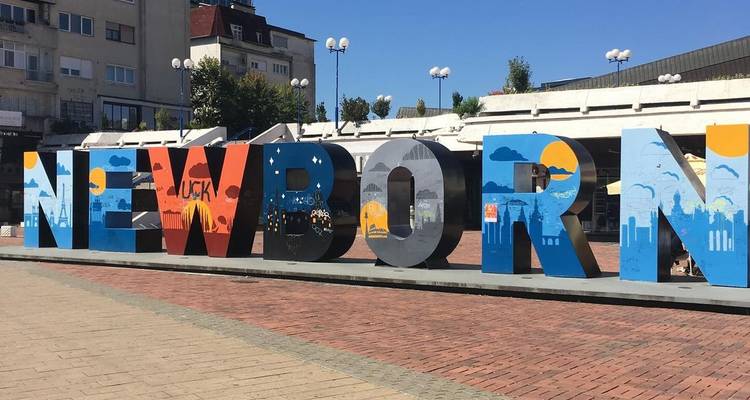 Das Denkmal „NEUGEBOREN" in fetten, bunten Buchstaben steht auf einem Stadtplatz unter einem klaren blauen Himmel.