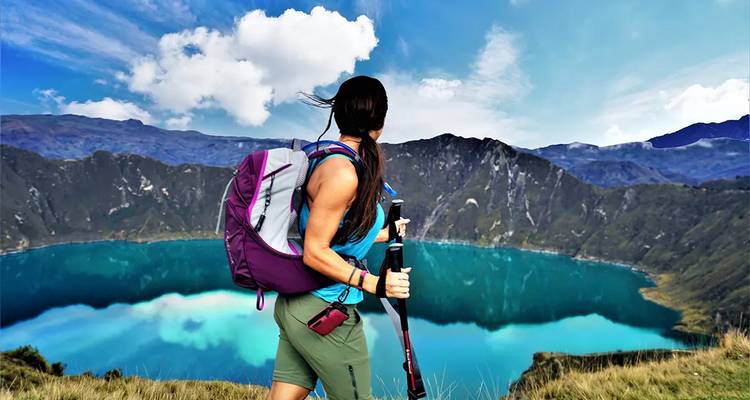 Excursionista femenina con mochila contemplando el brillante lago turquesa del cráter de Quilotoa desde una cresta alta.