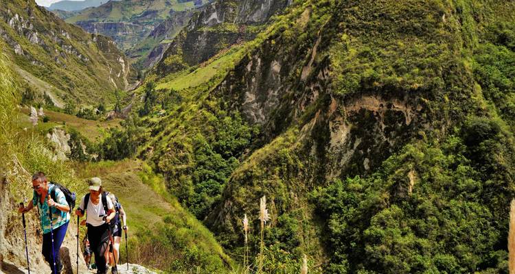 Wandelaars die een rotsig canyonpad beklimmen omringd door steile groene rotswanden in de Andes.