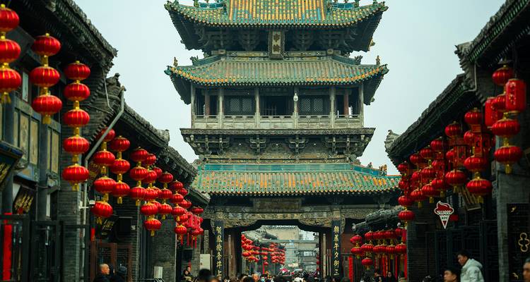 Mit Laternen gesäumte Straße, die zu einem verzierten antiken Turm in Pingyao führt, voller Besucher.