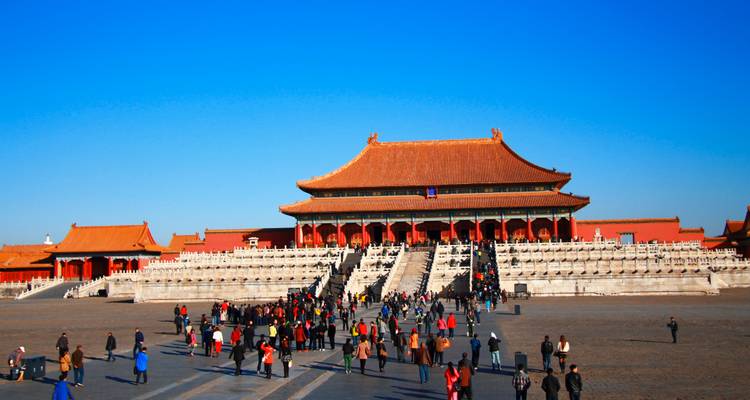 Toeristen beklimmen brede stenen trappen naar de grote hal van de Verboden Stad in Peking onder een heldere blauwe hemel.