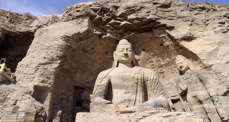 Enormes Budas de piedra tallados en la escarpada cara del acantilado de las Grutas de Yungang bajo el cielo azul.