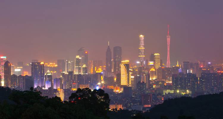 Verlichte wolkenkrabbers en Canton Tower die de avondnevel boven een uitgestrekte metropool doen oplichten.