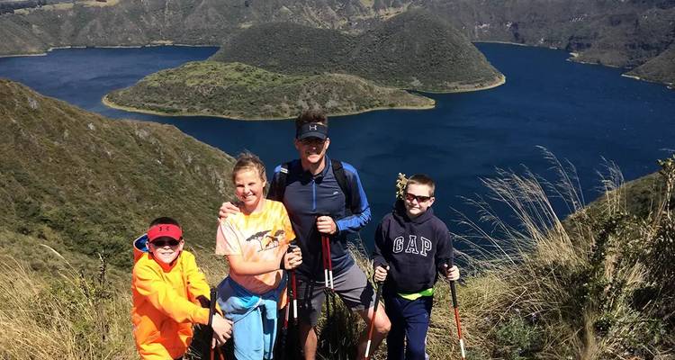 Familia sonriente de excursionistas posando en la cresta con vista al profundo lago azul del cráter Cuicocha.