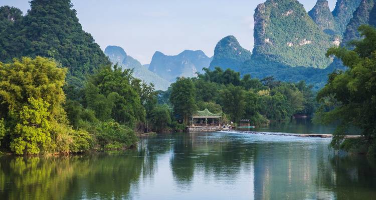 Río sereno reflejando dramáticos picos de karst de piedra caliza cubiertos de vegetación exuberante cerca de Guilin.