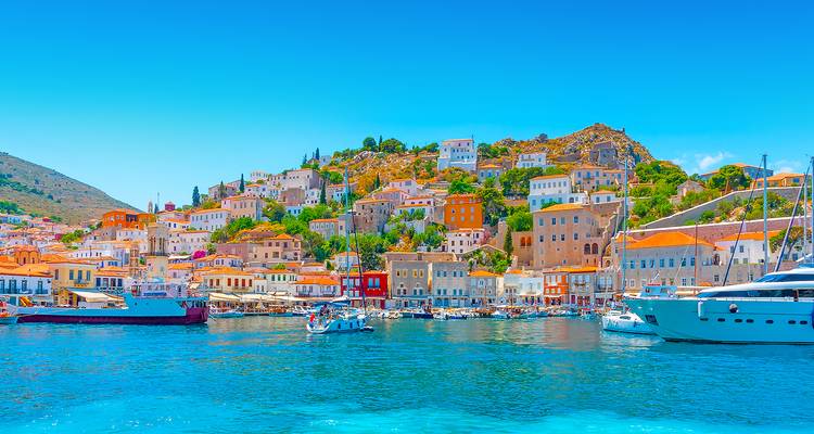 Ville colorée à flanc de colline surplombant un port bleu cristallin sous un ciel d'été lumineux.