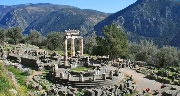Ruine circulaire du Tholos de Delphes au milieu d'un paysage montagneux avec des blocs de pierre anciens éparpillés alentour.