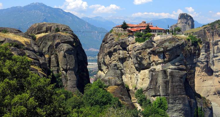 L'emblématique monastère des Météores se dresse au sommet d'imposants piliers de grès avec des montagnes lointaines sous un ciel bleu.