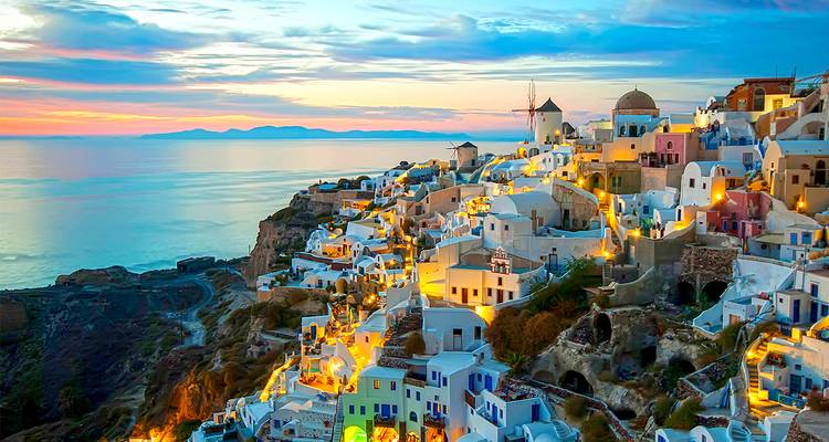 Le village d'Oia à Santorin brille de lumières dorées au crépuscule, ses maisons blanches dégringolant le long des falaises vers la mer Égée.