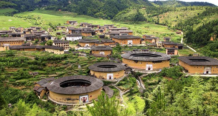 Panoramisch uitzicht op meerdere ronde Fujian tulou aarden gebouwen genesteld in weelderig landschap.