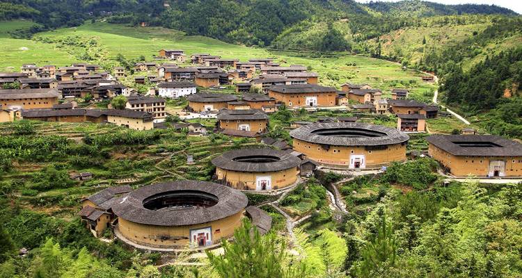 Panoramisch uitzicht op de heuvel met ronde aarden tulou-gebouwen verspreid tussen weelderige terrassen in Fujian