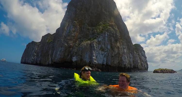 Dos personas haciendo snorkel flotando cerca de los acantilados dramáticos de Kicker Rock en mar abierto.