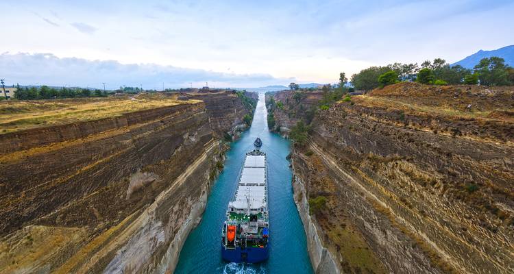 Barco de carga navegando por el estrecho Canal de Corinto de paredes empinadas con agua turquesa.