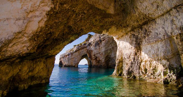 Zonovergoten natuurlijke bogen van de Blauwe Grotten van Zakynthos die boven het sprankelende water uitrijzen.