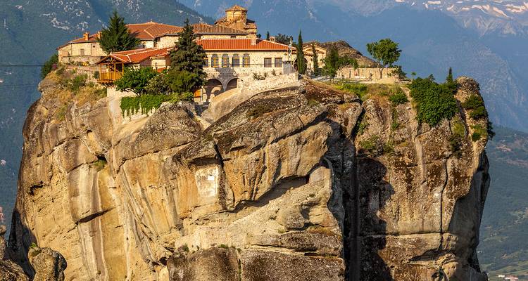 Klooster gelegen bovenop een dramatische zandstenen zuil in Meteora met bergachtergrond.